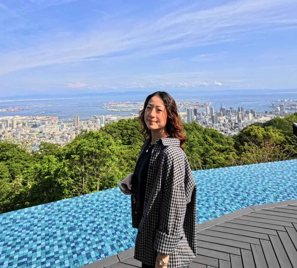 Nicole standing by an infinity pool overlooking a city and the sea